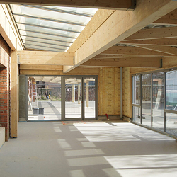 Intérieur en construction avec charpente bois, puits de lumière et baies vitrées