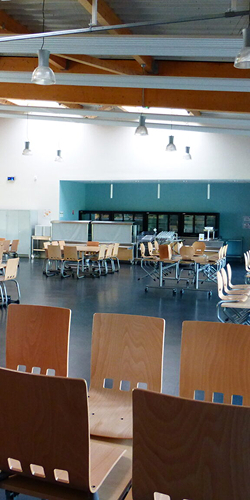 Réfectoire lumineux avec tables et chaises en bois clair et poutres apparentes