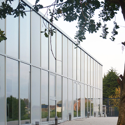 Façade vitrée moderne reflétant le ciel, encadrée par la verdure